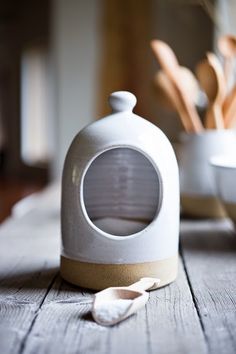 a white ceramic container sitting on top of a wooden table next to bowls and spoons