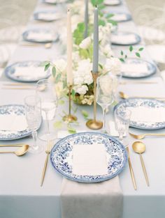 the table is set with blue and white plates, silverware, candles, and flowers