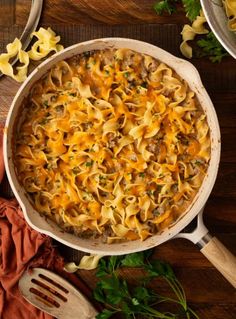 a casserole dish with meat and cheese in it on a wooden table next to utensils