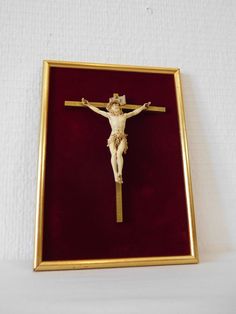 a gold framed crucifix with a red velvet case on the bottom and white wall behind it