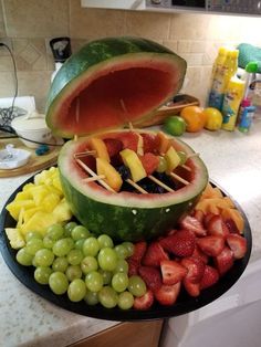 a watermelon is cut into pieces and placed on a platter with grapes, strawberries, melon, pineapple, grapefruit, kiwitch