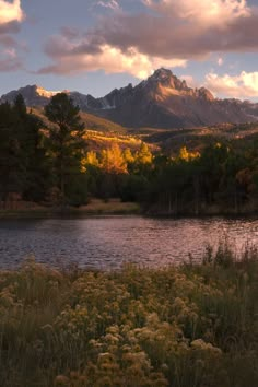 a lake surrounded by mountains and trees under a cloudy sky with clouds in the background