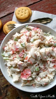 a white bowl filled with chicken salad next to crackers and a fork on the side