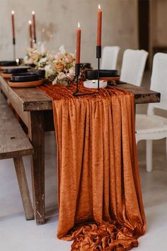 the table is set with candles, plates and napkins on top of an orange cloth