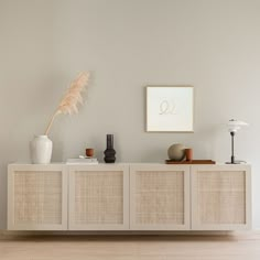 a white cabinet with two vases and a feather on top in a living room