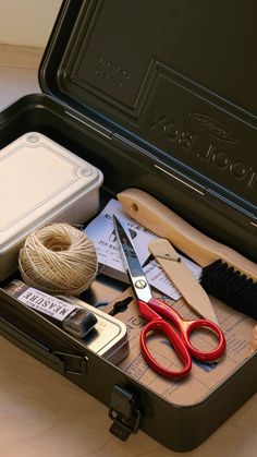 an open suitcase with scissors, yarn, and other items in it on a table