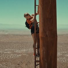 a woman climbing up the side of a tall metal structure in the desert with no one on it