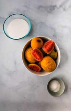 a bowl filled with sliced tomatoes next to a bowl of yogurt on a marble counter top