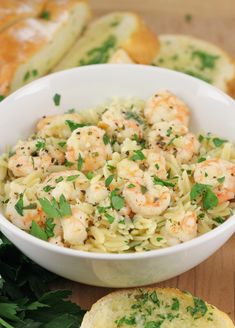 pasta with shrimp and parsley in a white bowl on a wooden table next to bread