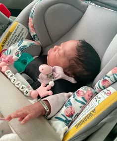 a baby laying in a car seat with stuffed animals on it's arm and head