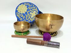 two singing bowls and a wooden mallet on a white surface