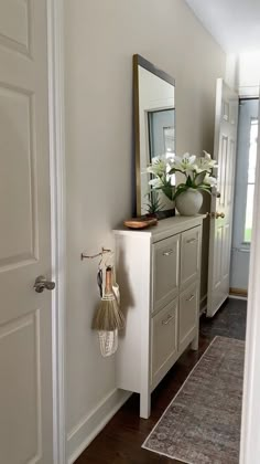 a hallway with a mirror, cabinet and flowers