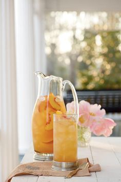 two pitchers filled with orange juice sitting on top of a wooden table next to flowers