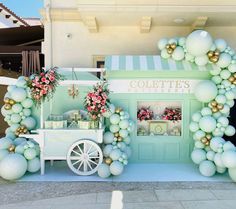 an ice cream cart is decorated with balloons and greenery for a dessert shop display