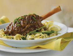 a white plate topped with meat and pasta covered in sauce next to lemon wedges