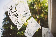 white paper cutouts hanging from the side of a building with trees in the background