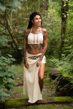 a woman with tattoos standing in the woods wearing a white skirt and halter top