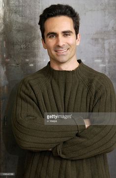 a man with his arms crossed posing for a photo in front of a metal wall