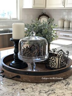 a tray with pine cones and candles on it in the middle of a kitchen counter