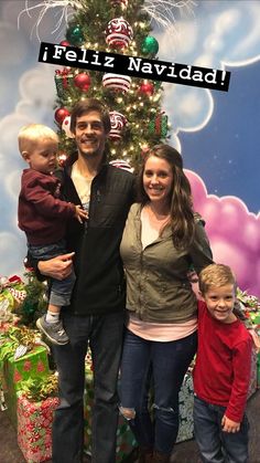 a man, woman and two children standing in front of a christmas tree with the words feliz navidad on it