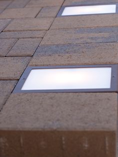 three square windows on the side of a brick building with white light shining through them