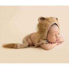 a baby sleeping on its side wearing a lion hat and diaper with long hair