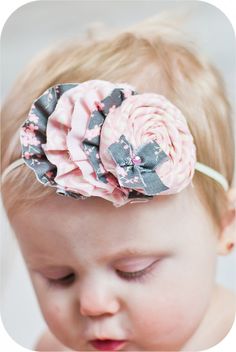 a baby girl wearing a pink and black flower headband with her eyes closed to the side