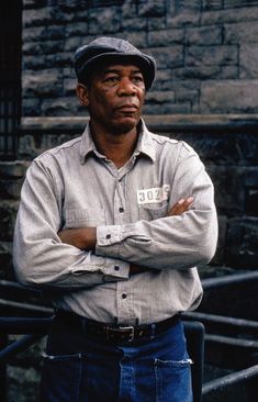 a man standing with his arms crossed and looking at the camera while wearing a hat