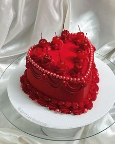 a red heart shaped cake with cherries on the top is sitting on a glass plate