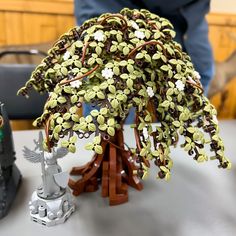 a miniature tree is sitting on a table next to a small figurine that looks like it's made out of legos