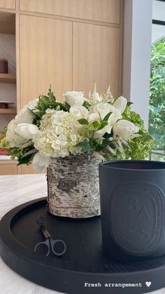 white flowers are in a vase on a black tray