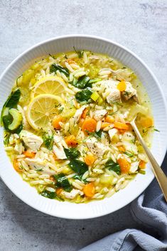 a bowl of chicken noodle soup with lemons, carrots and spinach