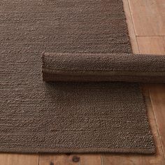 a brown rug is laying on the floor next to a wooden floor with a roll of fabric