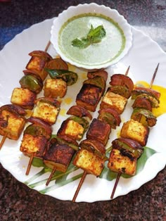 several skewers of food on a plate next to a bowl of dipping sauce