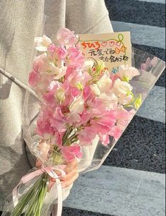 a person holding a bouquet of pink and white flowers in front of a sign with japanese writing on it