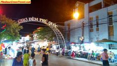 people are walking down the street in front of an open air market area at night