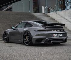 a grey porsche sports car parked in front of some stairs and steps with the door open