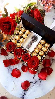 a box filled with red roses next to a bunch of chocolates and flowers on a table