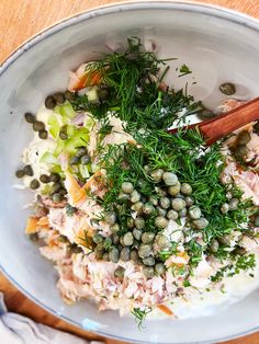 a white bowl filled with lots of food on top of a wooden table next to utensils