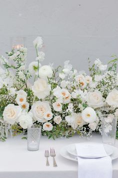 the table is set with white flowers and silverware