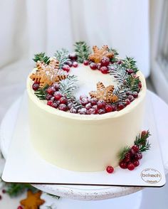 a white cake with cranberries and pine cones is on a platter next to other christmas decorations