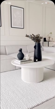 a white table with vases on top of it in front of a couch and mirror