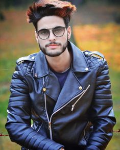 a man in black leather jacket and glasses sitting on a bench with his arms crossed