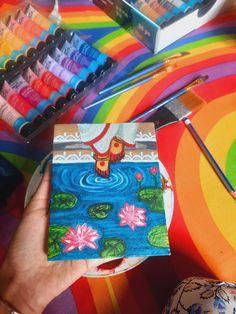 a person holding a small piece of art paper in front of colorful paintings and water lilies