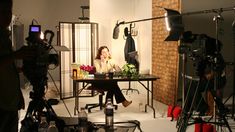 a woman sitting at a table in front of a camera set up for a photo shoot