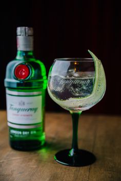 a bottle of gin and a wine glass on a wooden table with a green light behind it