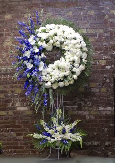 white and blue flowers are arranged in front of a wreath on a brick building wall