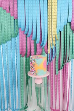 a cake sitting on top of a table in front of colorful ribbons hanging from the ceiling