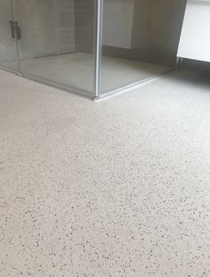 a bathroom with white flooring and a glass shower stall in the corner on one side