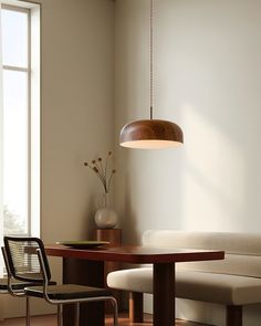 a room with a table, chair and lamp hanging from it's ceiling in front of a window